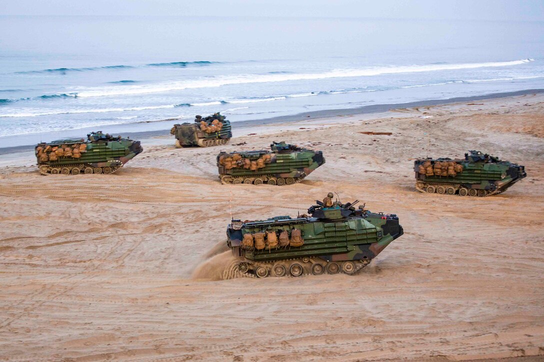 Marines drive five amphibious assault vehicles on a beach.