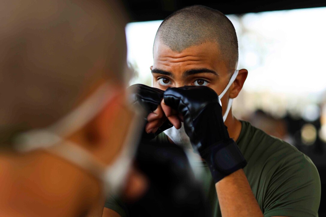 A Marine Corps recruit wearing boxing gloves holds his hands up to his face.