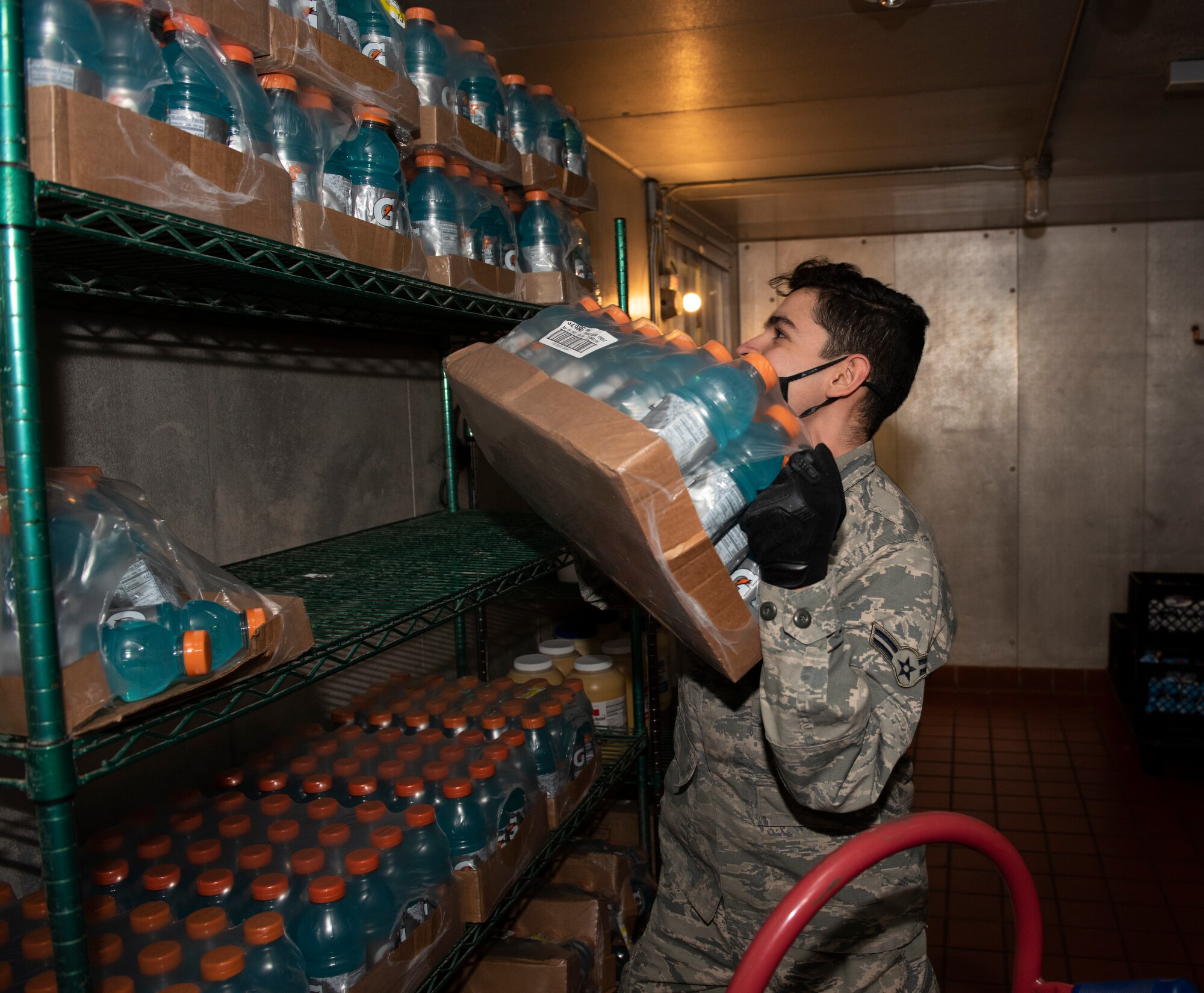 An Airman picks up a box of Gatorade to store in a walk in freezer.