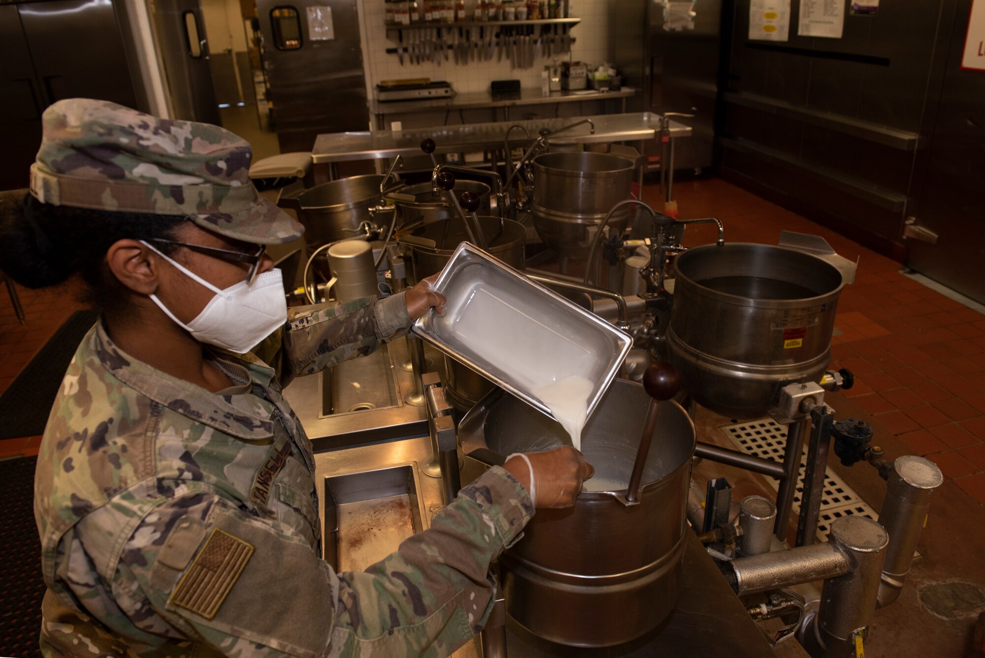 A sergeant pours corn starch into a steam kettle.