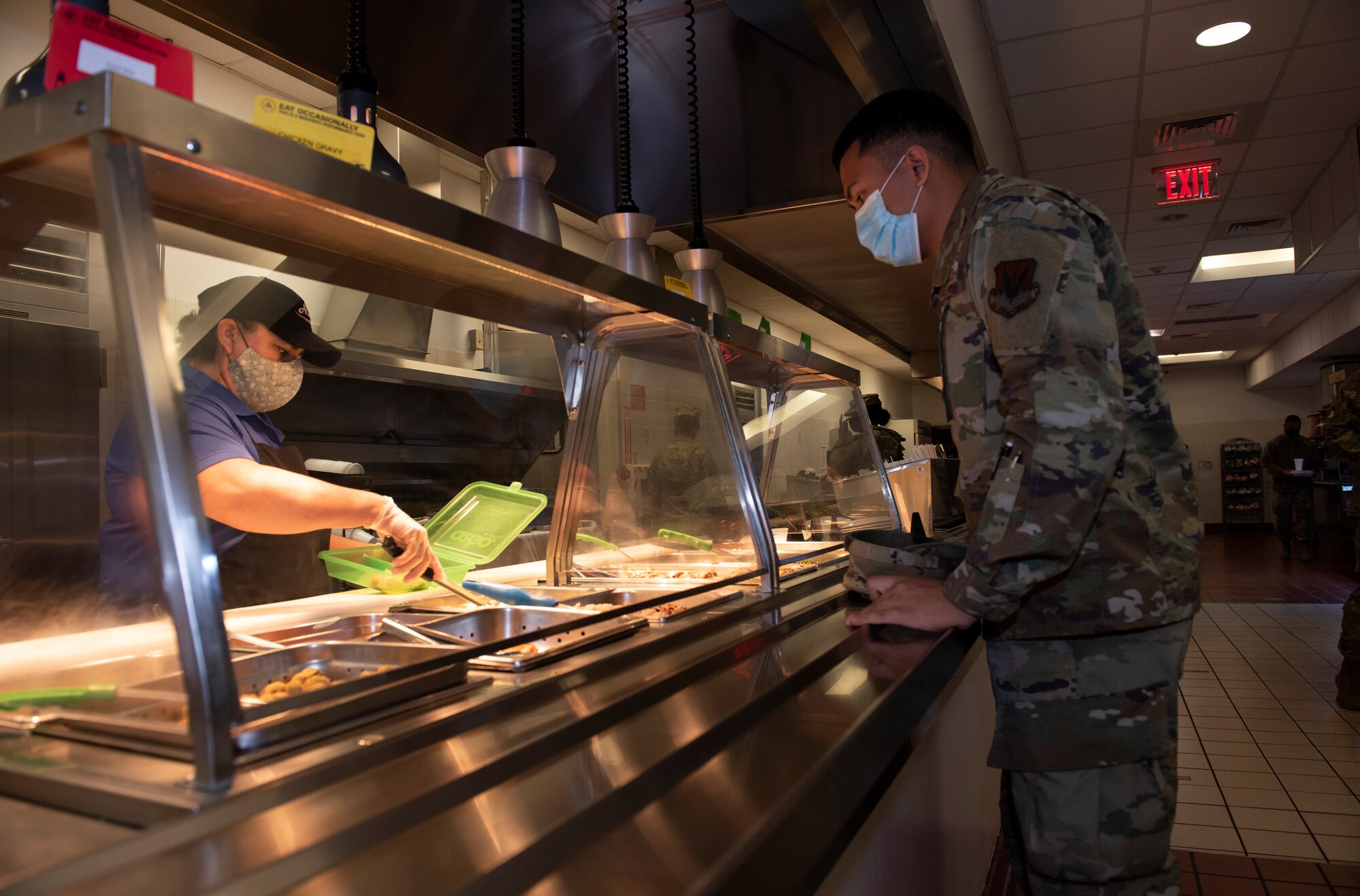 A worker gives a to-go plate, filled with food inside, to an Airman.