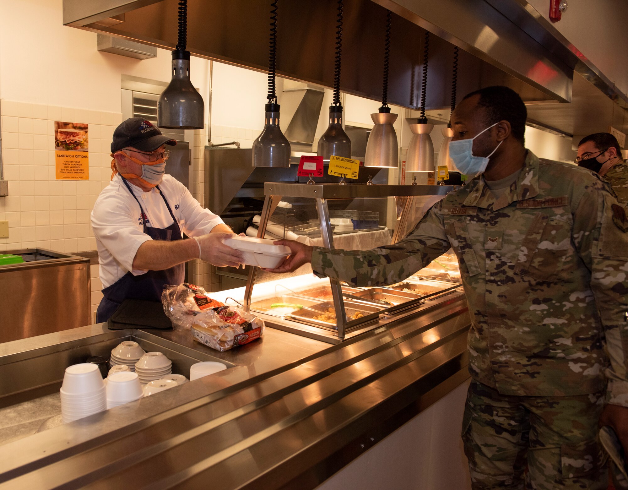 A worker gives an Airman his to go plate filled with food inside.