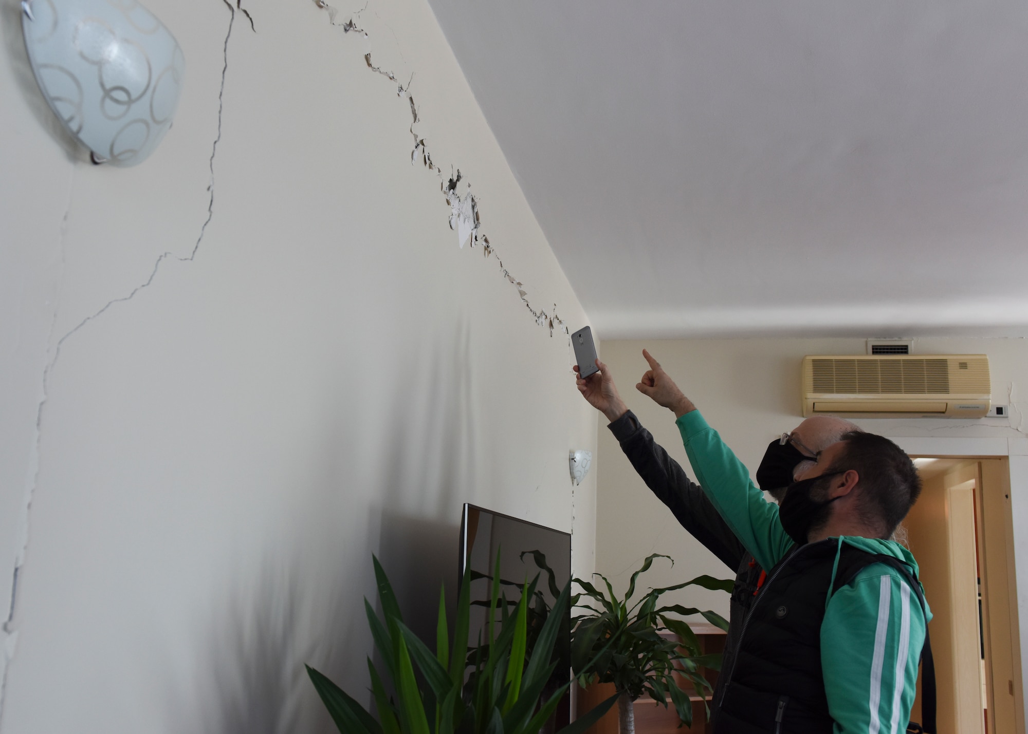 Two men pointing at a damaged wall