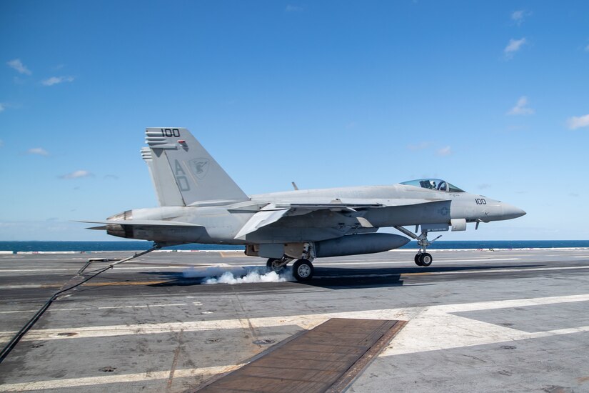 A military aircraft lands on the deck of a ship.