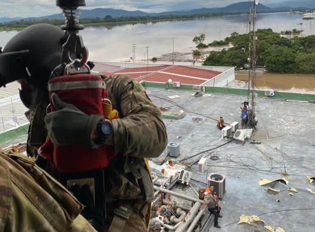 A soldier hangs outside a helicopter over a heavily flooded area.