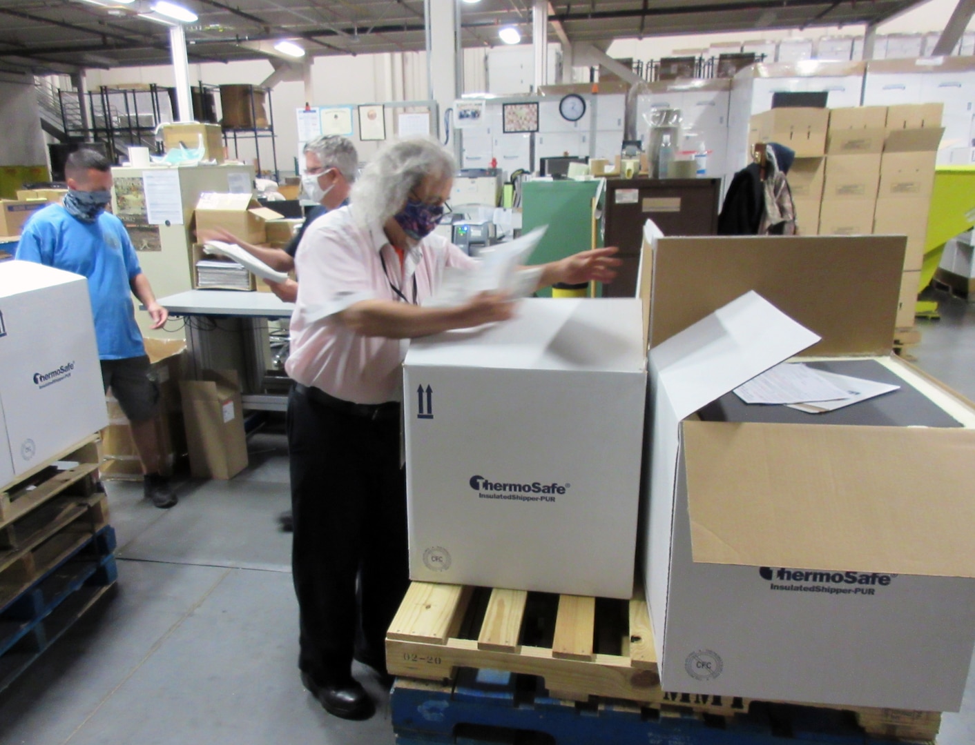 Masked warehouse workers inspect boxes of hand sanitizer stacked on a pallet