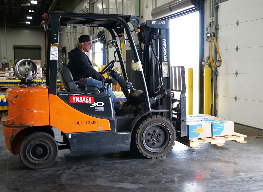 A forklift operator moves a pallet of gowns in a warehouse