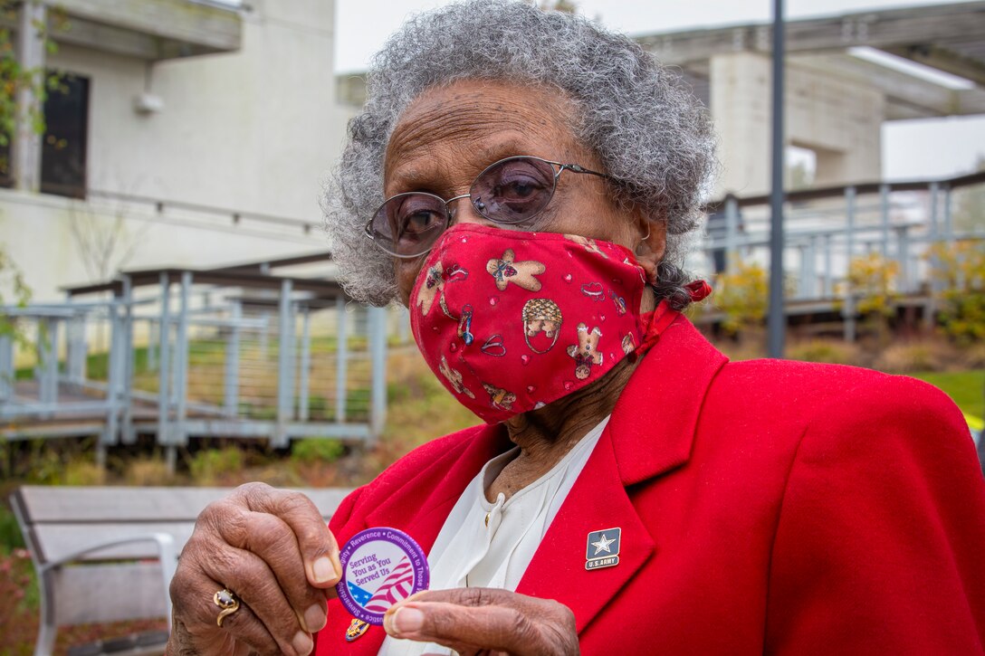 An older woman in a mask holds up a coin.