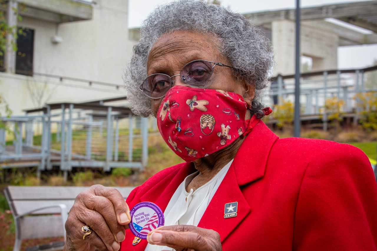 An older woman in a mask holds up a coin.