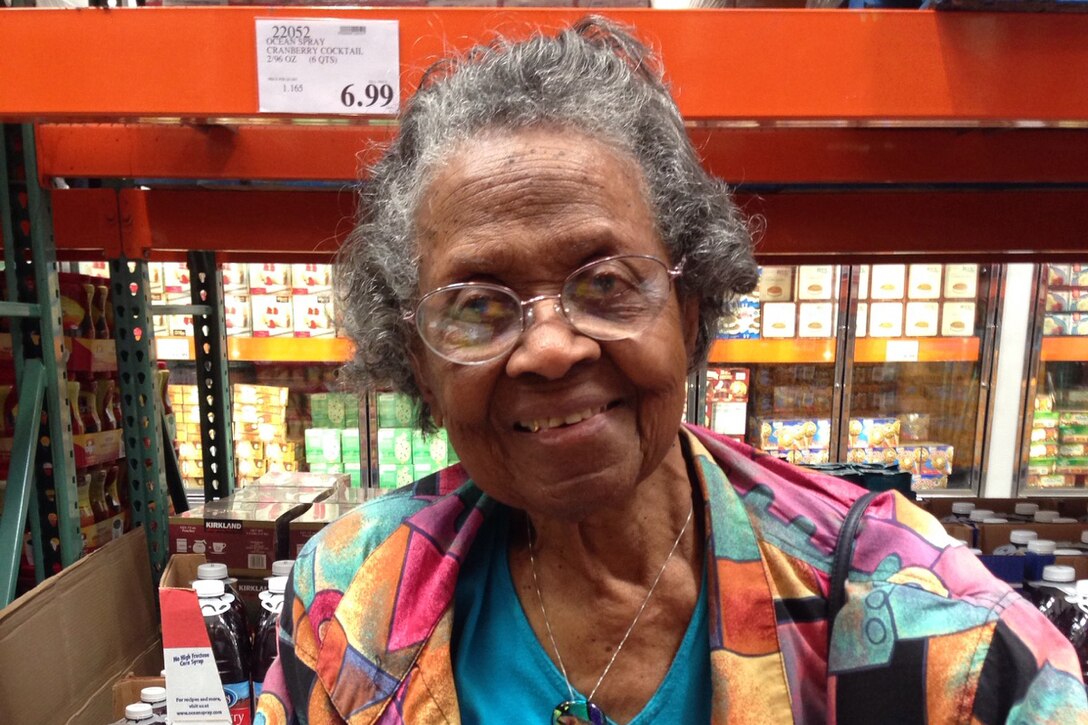A woman pushing a shopping cart stands in a warehouse filled with food products.