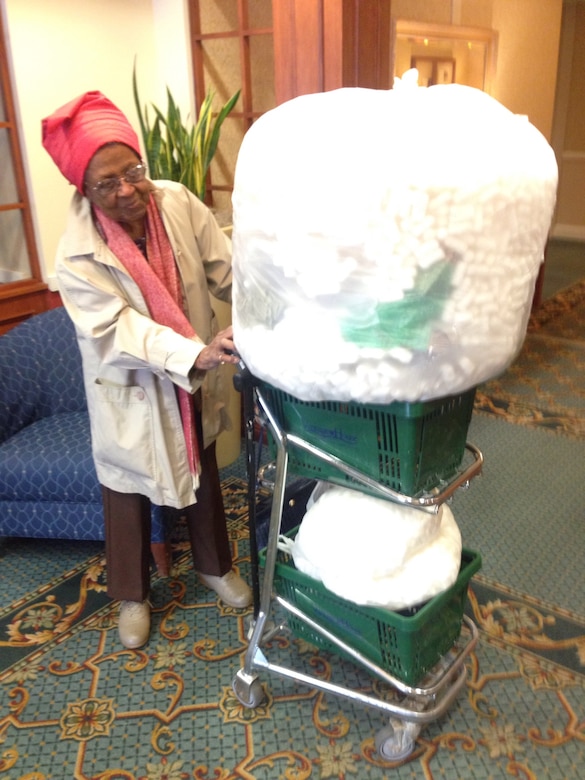 A woman pushes a shopping cart filled with two massive bags of packing peanuts.