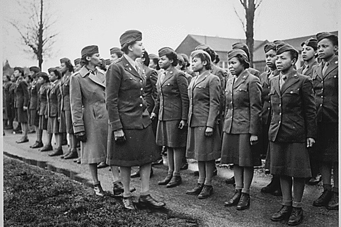 Rows of Black women in uniform stand in formation while two other women address them.