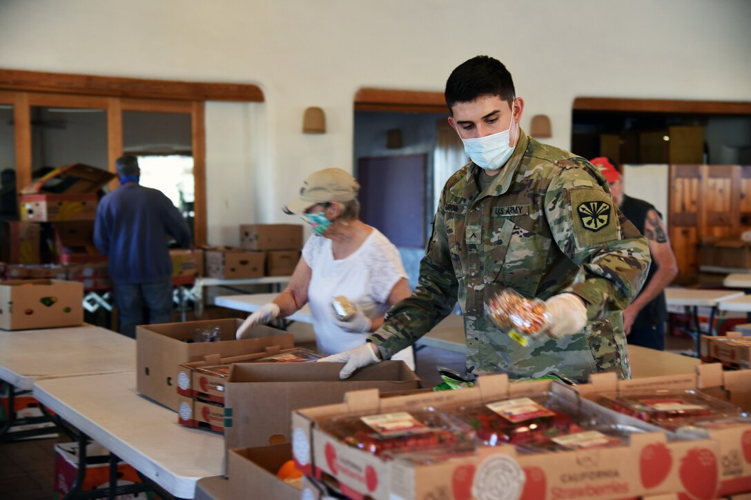 A soldier wearing a face mask and gloves puts food into a box.