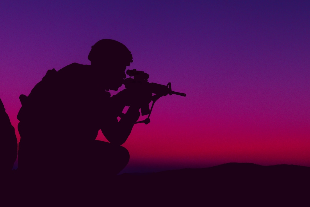 A Marine shown in silhouette aims a weapon under a pink and purple sky.