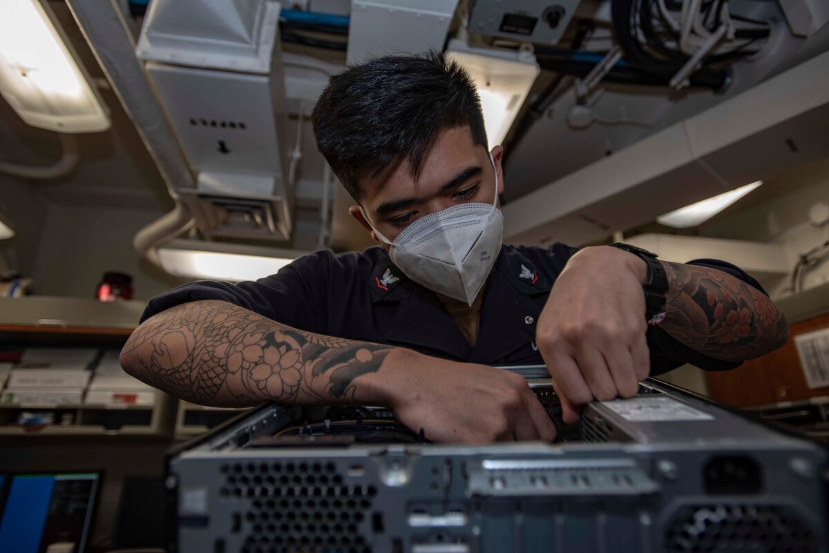 A sailor does maintenance work on a computer.
