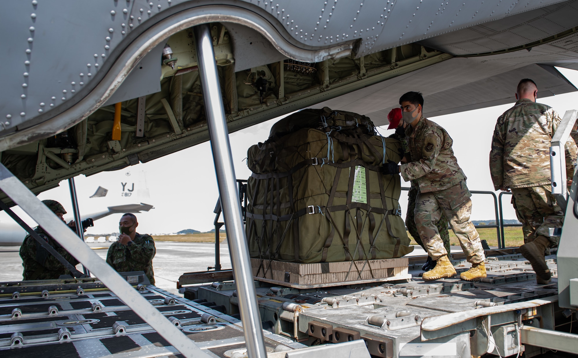 A Japan Self-Defense Forces member, center left, and a 374th Logistics Readiness Squadron Airman, center right, push a containerized delivery system bundle onto a C-130J Super Hercules