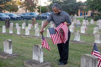 Naval Support Activity (NSA) Hampton Roads, Portsmouth Annex Site Director Kenneth Pugh placing flags at the gravestones of fallen service members at the Captain Ted Conaway Memorial Naval Cemetery in Naval Medical Center Portsmouth (NMCP) in honor of Veterans Day.