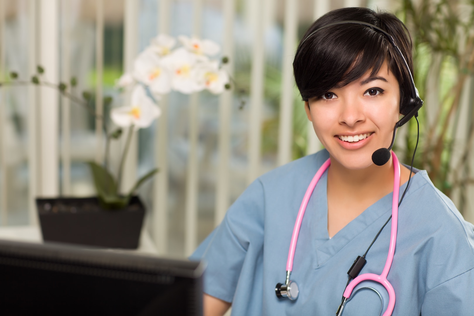 Smiling young woman with headset near her computer monitor.