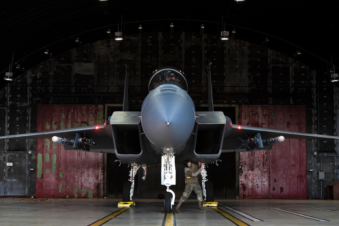 An airman stands under an aircraft in a hangar.