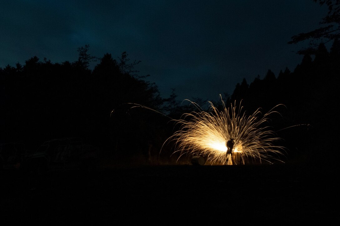 Sparks fly as an airman cuts into a metal barrel.