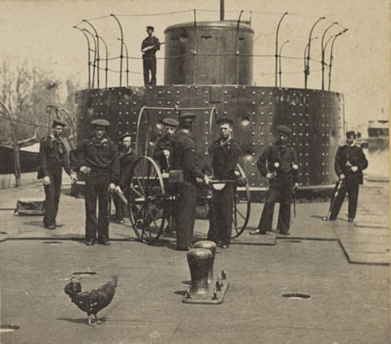 An old photo shows sailors standing in front of a turret on a ship.