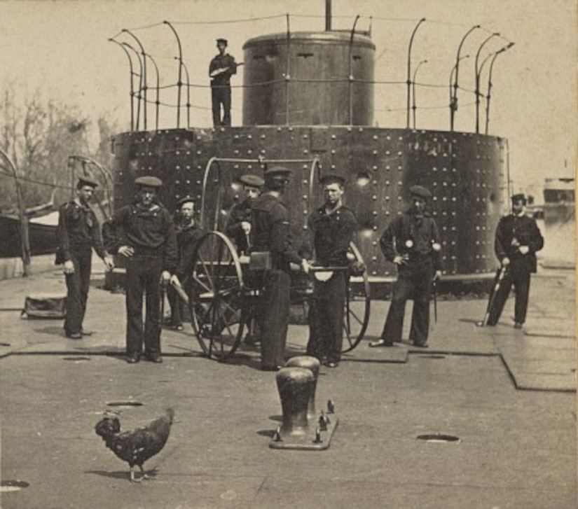 An old photo shows sailors standing in front of a turret on a ship.