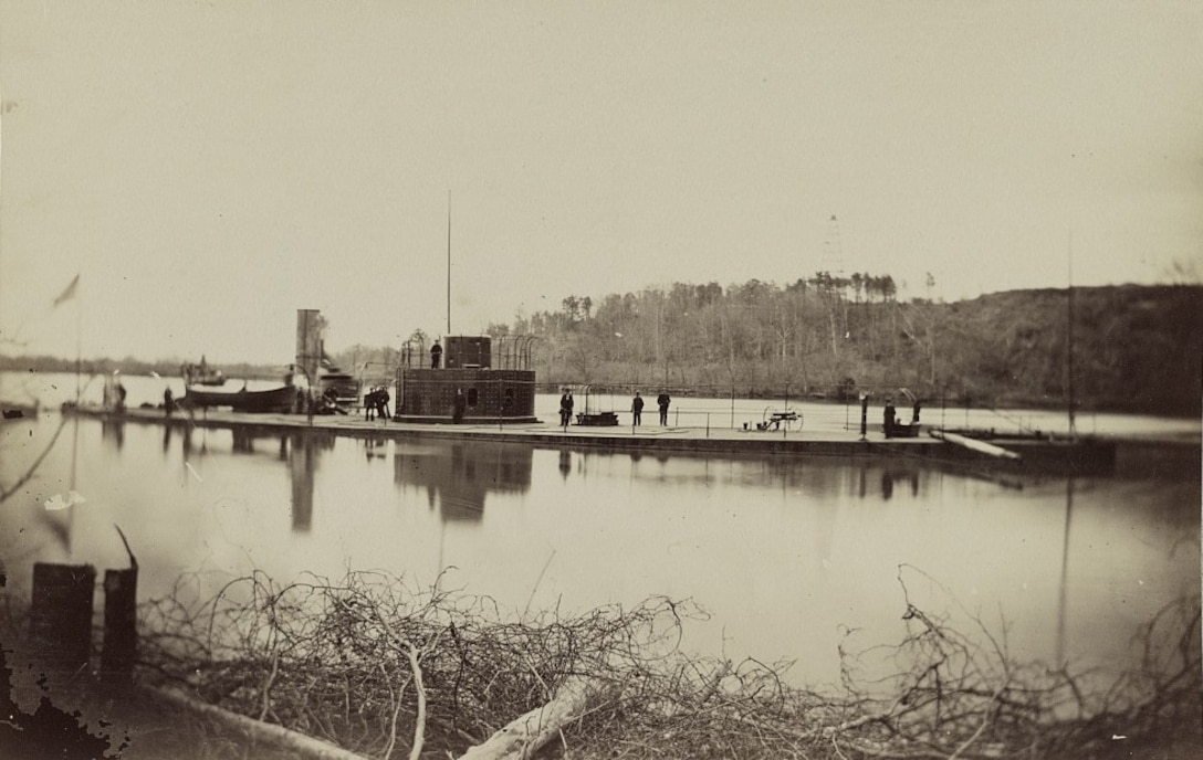 An ironclad Civil War ship’s deck is visible just above the water level on a river.
