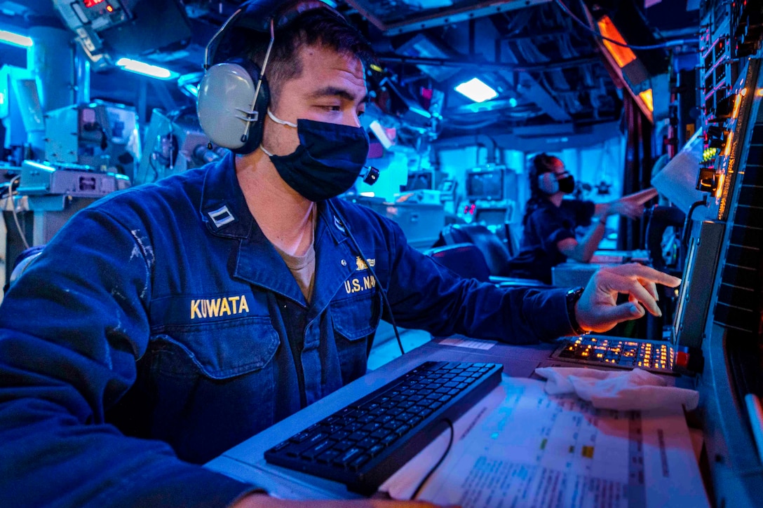 A sailor sits at a desk in front of monitors.
