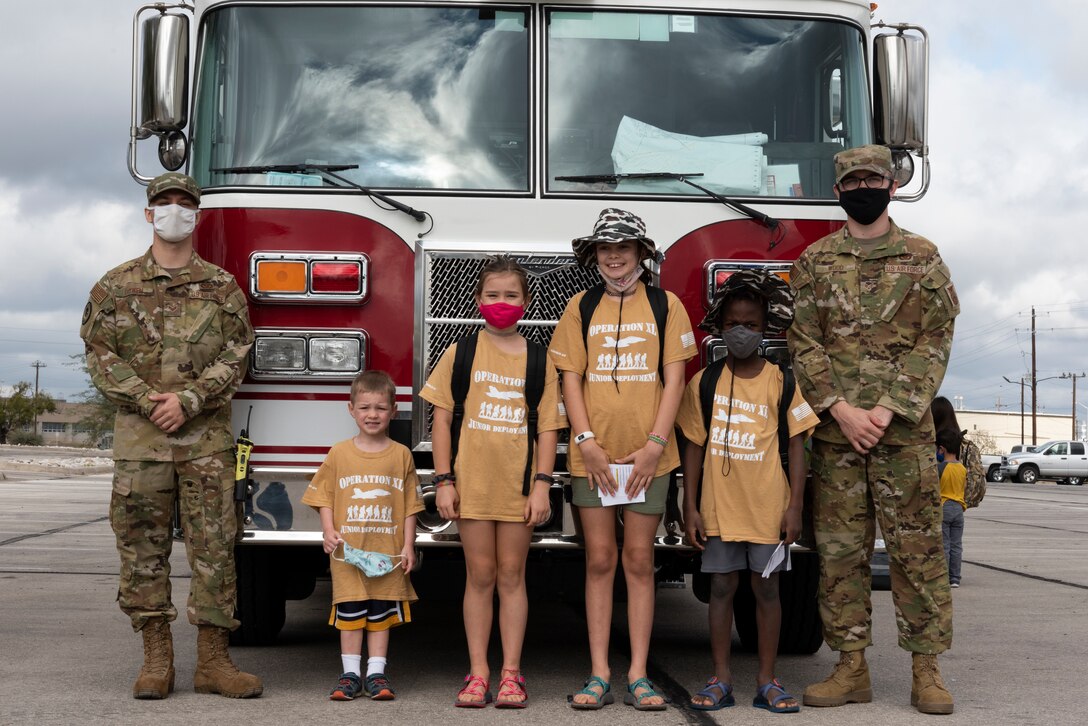 Senior Airmen Brodie Bowen and Carson Wood, 47th Civil Engineer Squadron firefighters, pose with junior deployers for a photo in front of a base fire truck on Nov. 7, 2020 at Laughlin Air Force Base, Texas. The fire truck was one of five stations the children visited during the Junior Deployment. (U.S. Air Force photo by Senior Airman Anne McCready)