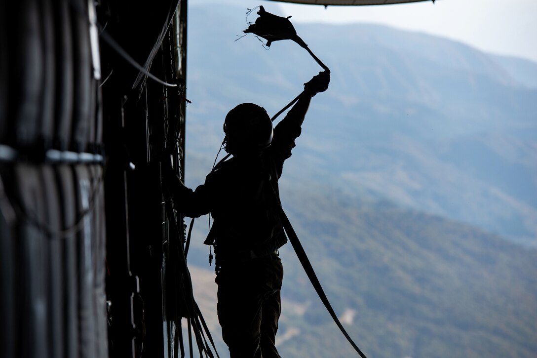 An airman shown in silhouette grabs a parachute line.