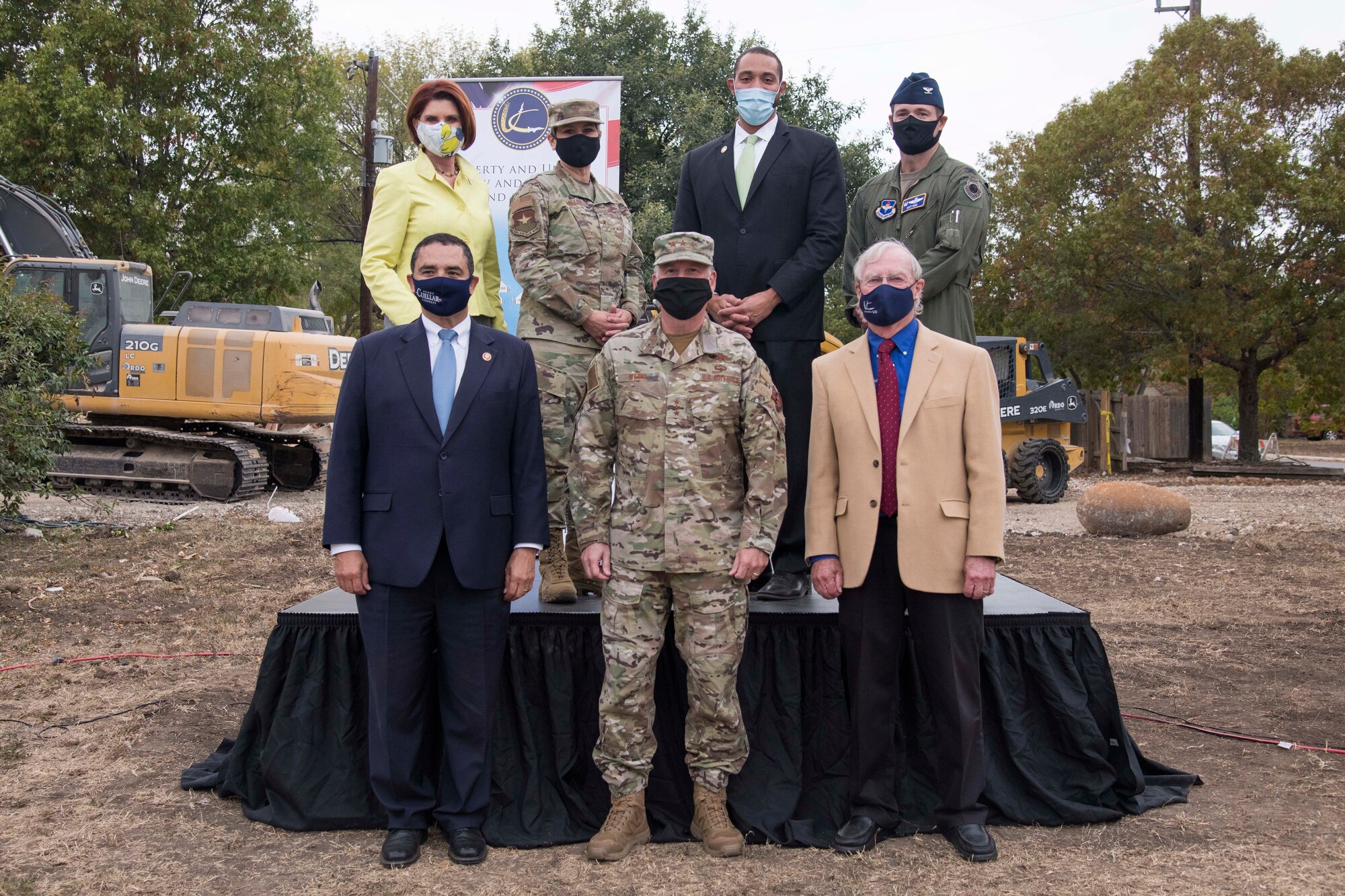 A group of people wearing masks, outdoors, in front of construction equipment.