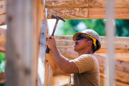 Construction Electrician 3rd Class Microneil Arellano, from Sacramento, Calif., deployed with the Seabee expeditionary construction and engineering capability of Task Force 75, installs hurricane straps to secure trusses in support of Southwest Asia hut construction on Camp Tinian.