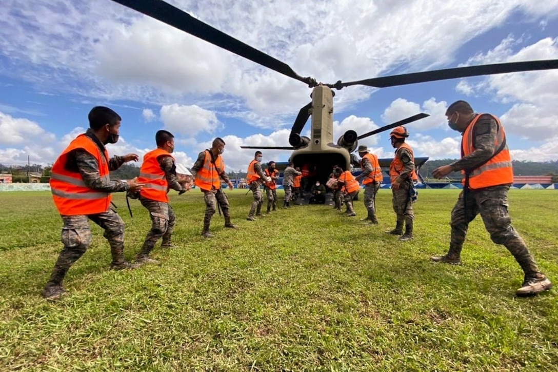 U.S. and Guatemalan troops wearing orange vests unload supplies from a helicopter.