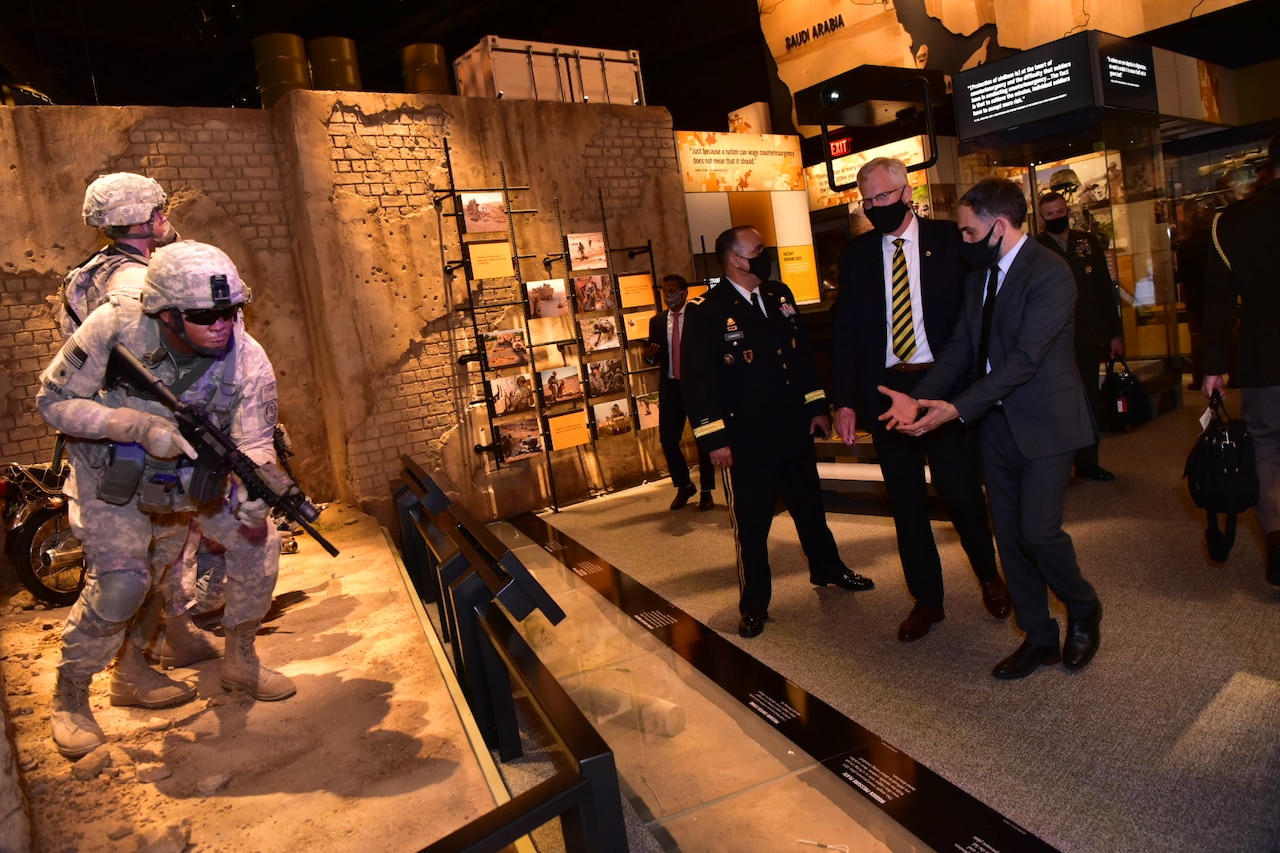 Three men stand near a museum exhibit that featureS models of soldiers who are carrying rifles.