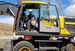 A man with a hard hat sit in the cab of a yellow piece of material handling equipment.