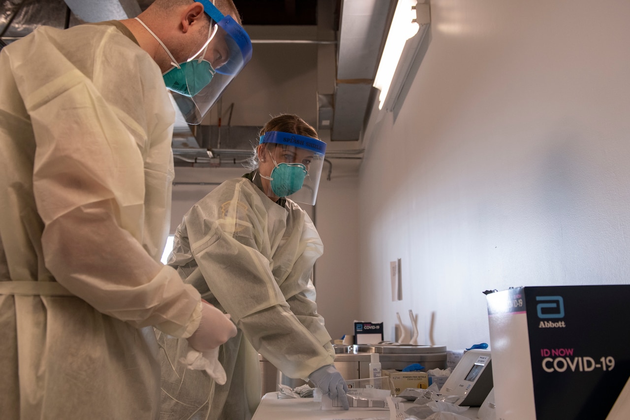 A man and a woman, both wearing protective equipment, prepare to administer a medical test.