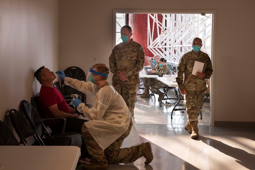 An airman stands by watching another airman administer a nasal swab test to a man.