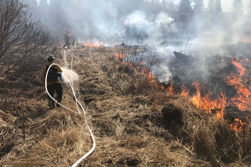 People spray water on a burning field.