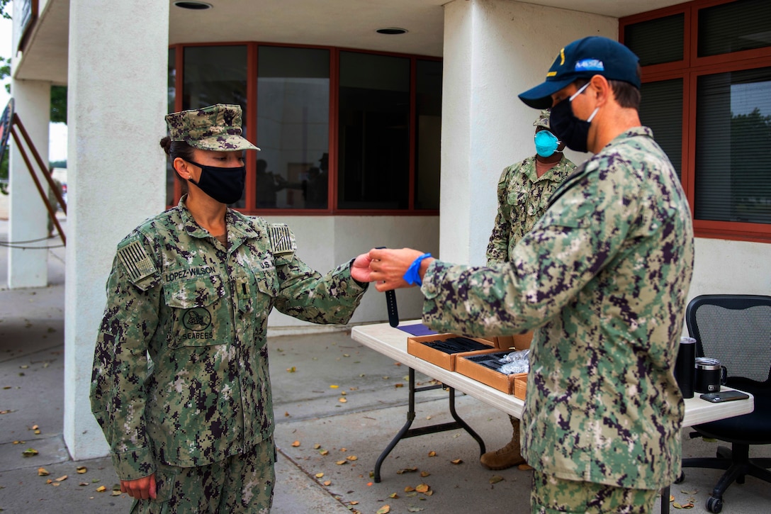 A sailor wearing a face mask hands something to a sailor wearing a face mask.