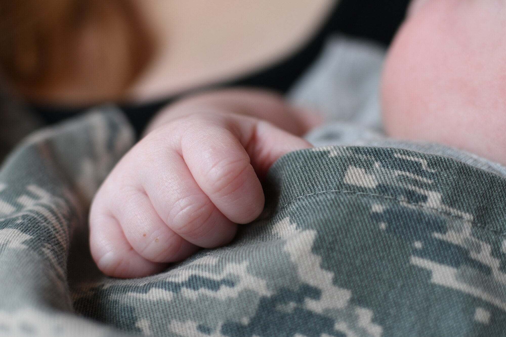 photo shows a baby hand gripping the should of of military uniform.