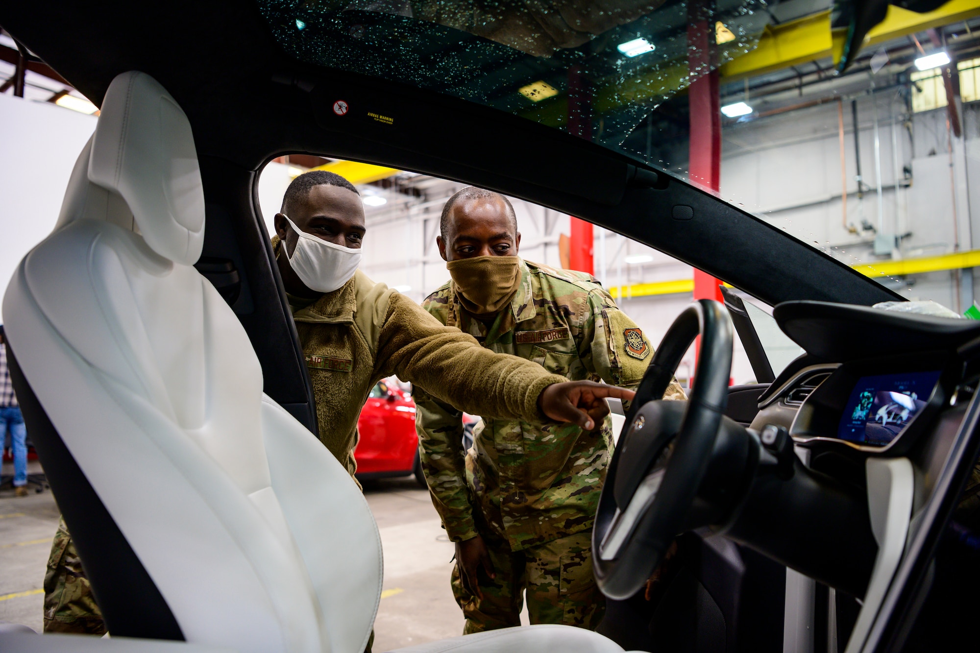 Two airmen look at the driver's side door of a Tesla Model X.