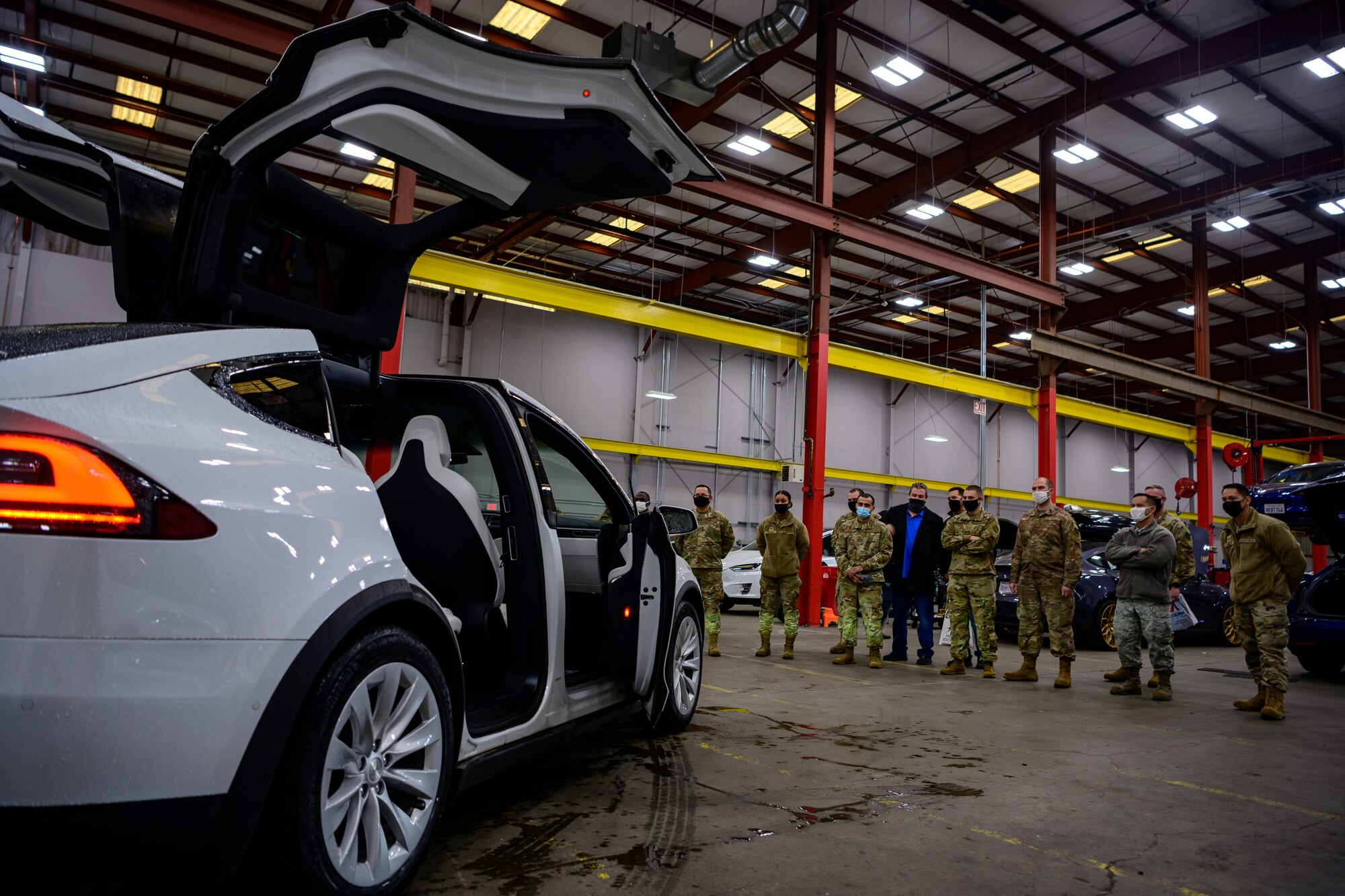 Airmen stand around a car and watch it automatically open its doors and flash its lights.