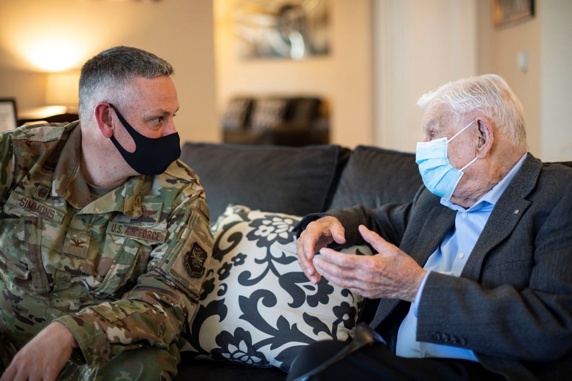 A man in a military uniform speaks to an older gentleman in a suit.