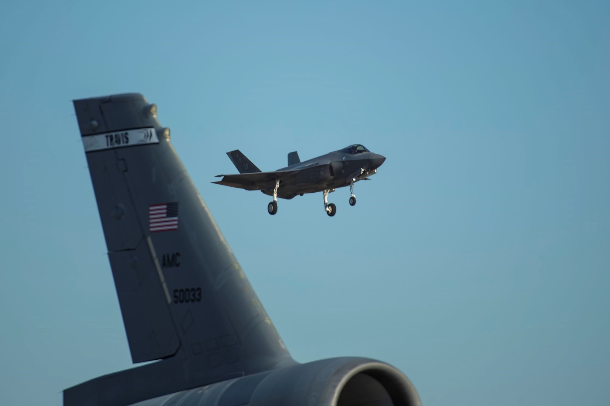 A fighter jet flies in the background. A Travis KC-10 Extender tail is in the foreground