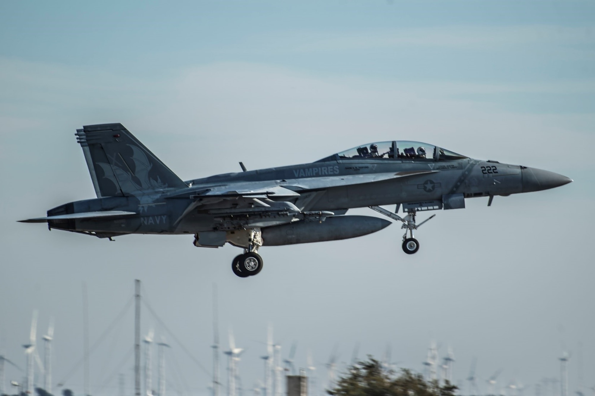 A fighter jet flies by as it approaches the ground for a landing.