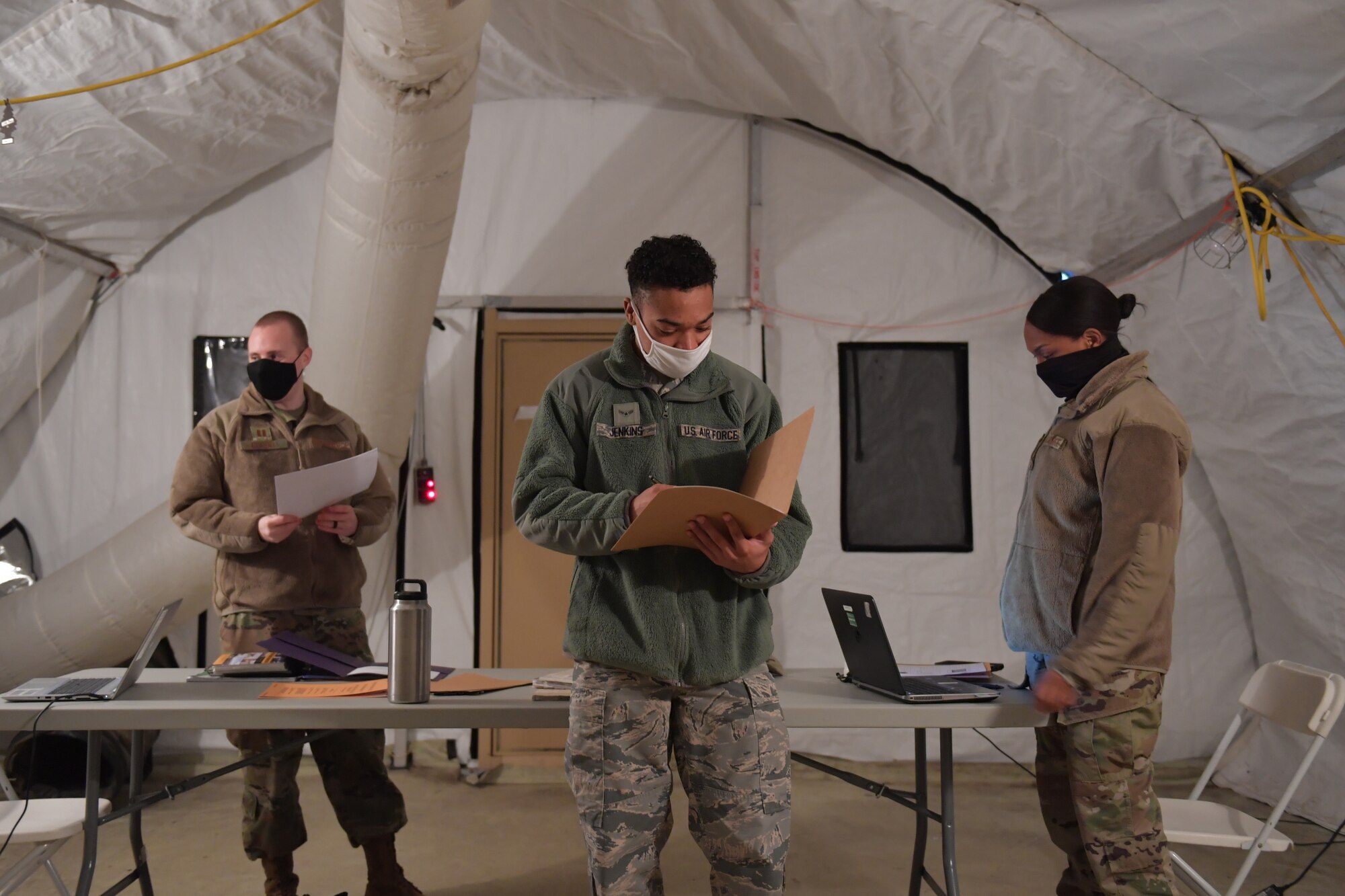 Three Airmen standing in a tent.