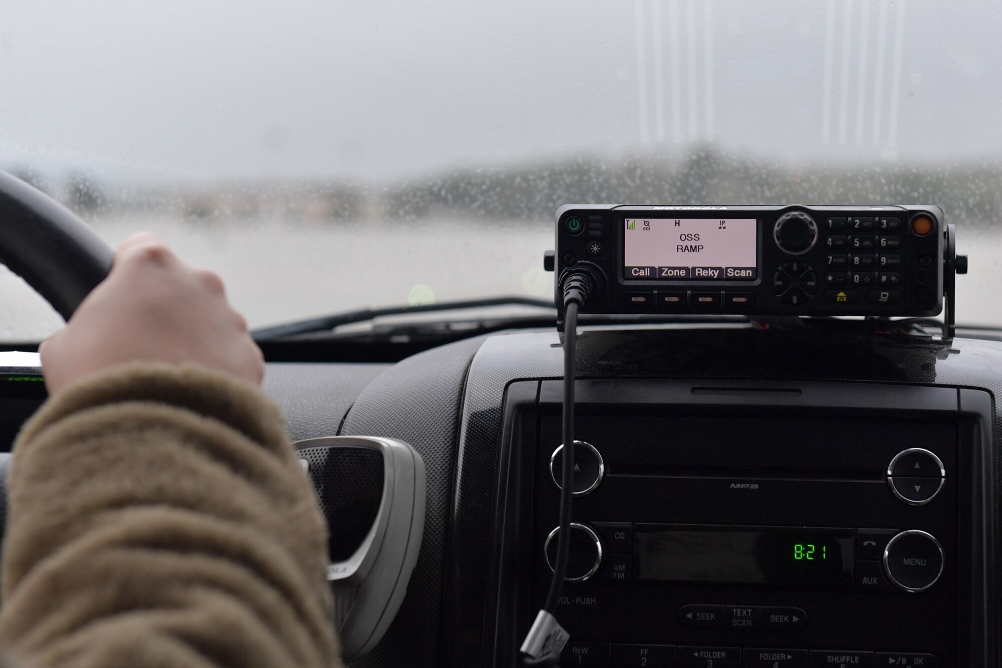 Close-up of a hand on a steering wheel and a radio receiver.