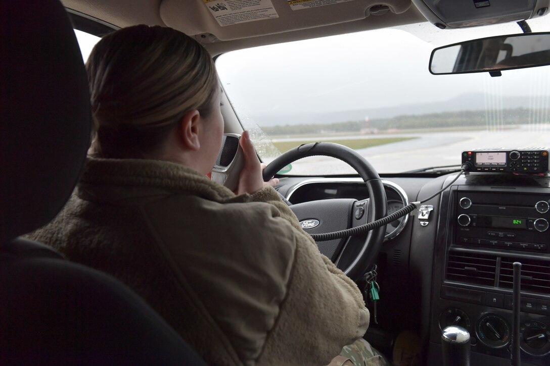 An Airman driving and holding a radio.