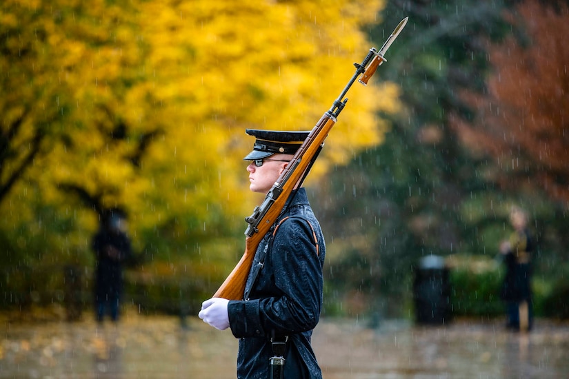 A soldier walks in the rain holding a rifle.