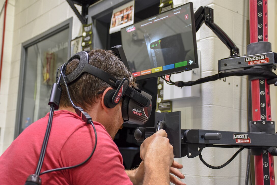 A man wears a virtual-reality headset and uses a sensor-based welding gun to weld in virtual reality.